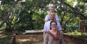 Three persons standing outdoors under trees